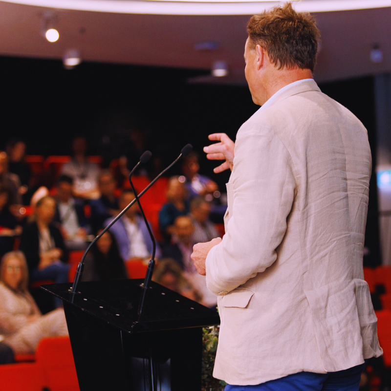 A photo of a man speaking to a crowd at a conference.