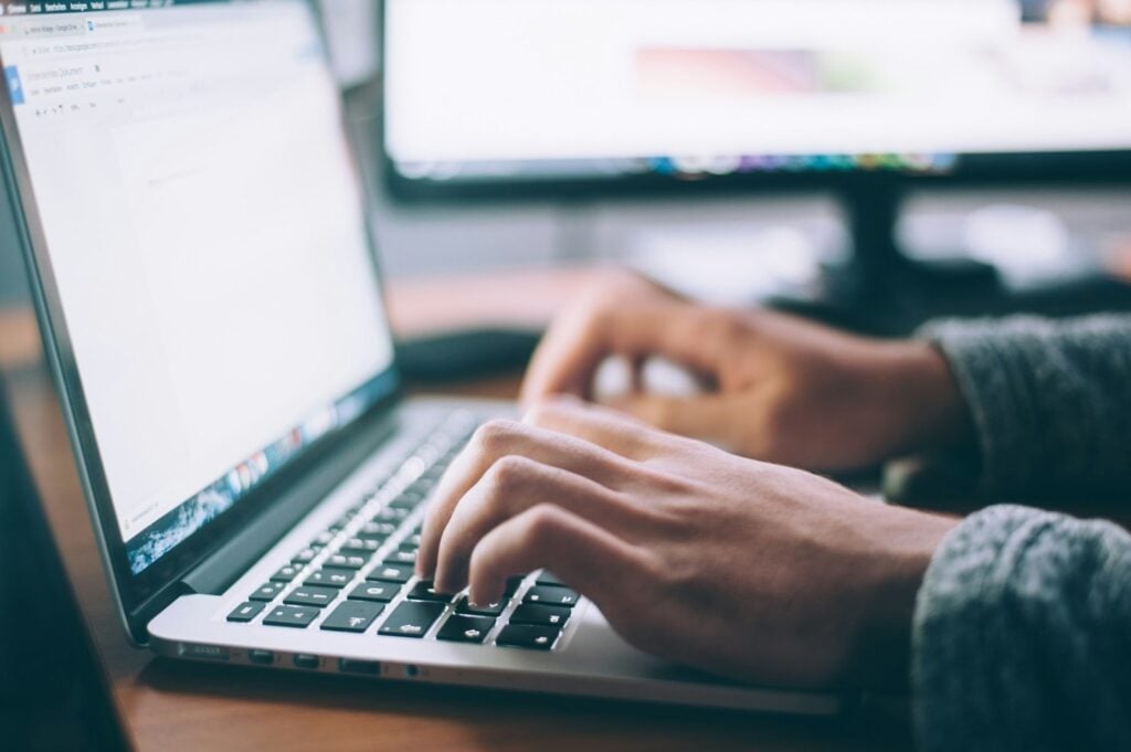 Close up photo of a person typing on a laptop. Only the person's hands are in view.