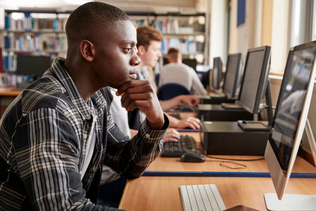 A photo of a man reading from a library computer.