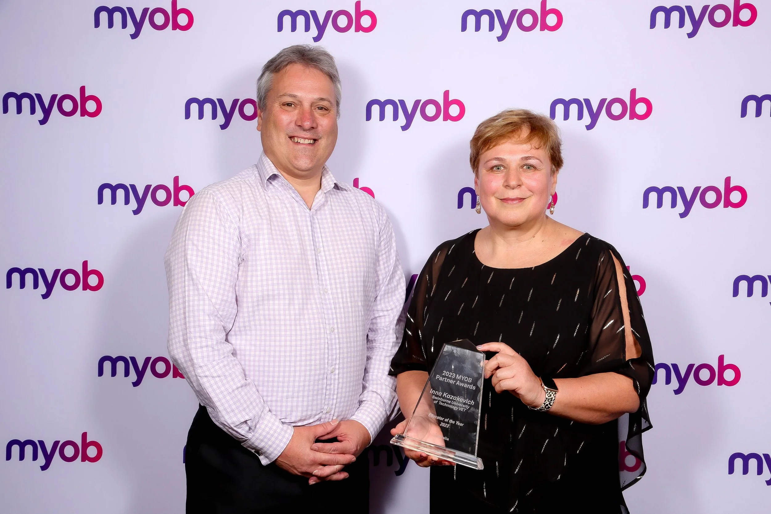 A photo of a man and woman smiling at the camera. The woman is holding an award trophy.